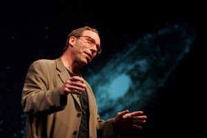 Dr. Lawrence Krauss with an image of a galaxy behind him.